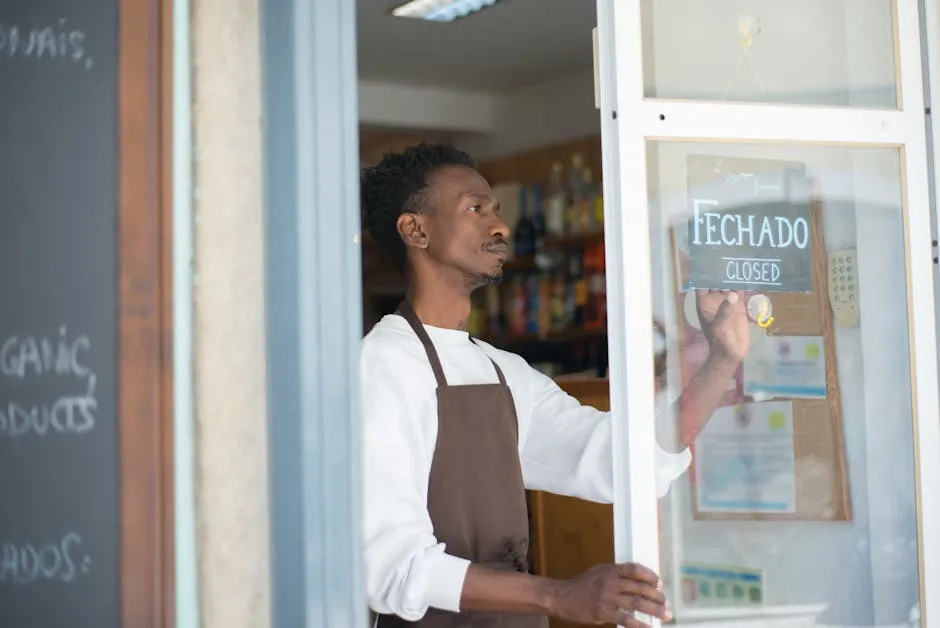 African man closing a store with a sign in Portuguese, wearing an apron.